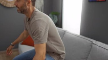 Genç adam şık bir oturma odasında rahat bir kanepede dinleniyor modern dekorun ve rahat yastıkların yer aldığı rahat, huzurlu bir ortam yaratıyor..