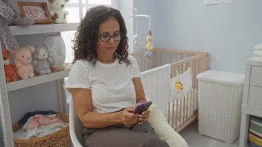 Bebek beşiği ve oyuncaklarla çevrili çocuk odasında oturan bir kadın, aile ortamında huzurlu bir ev ortamını ima ediyor..