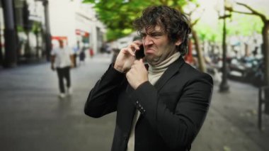 Dışarıda cep telefonuyla konuşan bir adam, şehir ortamında ifade edici bir yüz, ceketli, bulanık insanlar ve arka planda ağaçlar olan bir adam..