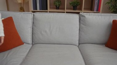 Kadın, rahat bir oturma odasında gri bir kanepe ve kırmızı yastıkla otururken, beyaz bir kazak ve kot pantolon giyerken, evdeki hayal kırıklığını ve endişeyi ifade ederken strese girdi..