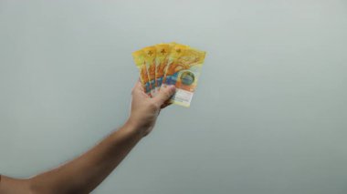 İsviçre frangı banknotları tutan bir adamın eli beyaz bir arkaplanda, izole bir ortamda para ve finans kavramlarını gösteriyor..