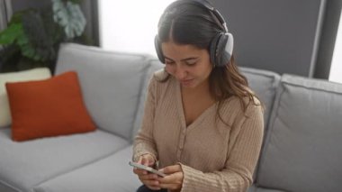 Kanepede dinlenen, kulaklık takmış, gözleri kapalı müzik dinleyen, rahat bir oturma odasında huzurlu bir anın tadını çıkaran bir kadın..