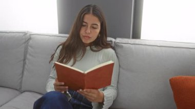 Oturma odasındaki rahat koltukta kitap okuyan bir kadın. Etrafı yastıklarla çevrili. İçeride huzurlu bir anın tadını çıkarıyor..