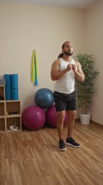 Spor salonunda egzersiz yapan bir adam, dayanıklılık bantları ve toplarla çevrili spor aletleri ve ahşap zeminle.