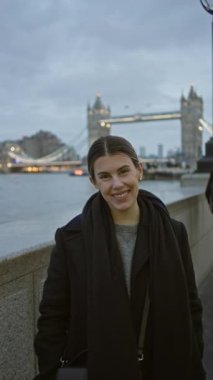 Londra 'da bulutlu bir günde ikonik kule köprüsünün önünde gülümseyen bir kadın canlı şehir hayatı ve tarihi mimari sergiliyor..