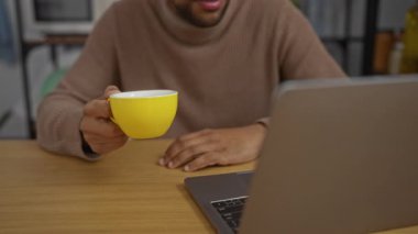 Ofisteki genç adam laptopuna odaklanmışken kahvesini yudumluyor. Etrafı modern dekor ve rahat bir atmosferle çevrili..