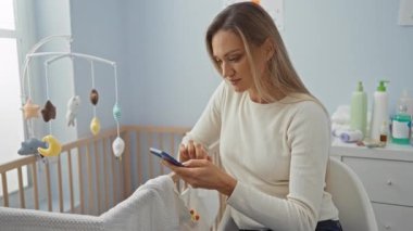Gündüz vakti evde otururken modern bebek odasında akıllı telefon kullanan bir kadın..