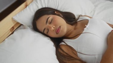 Yatakta, yatak odasında yüzü acı dolu bir ifadeyle yatan bir kadın. Tahta bir yatak başlığı ve beyaz bir yatak örtüsüyle.