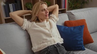 Oturma odasındaki kanepede dinlenen, rahat ev ortamında rahat bir şekilde gülümseyen, rahat yastıklar ve zarif dekorlarla, sükuneti ve rahatlığı somutlaştıran bir kadın..