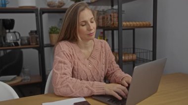 İş yerinde dizüstü bilgisayarını kapatırken gülümseyen bir kadın, arka planda raflarla birlikte, işten sonra rahat bir ortamda pembe kazak ve uzun saçlı bir şekilde rahatlamayı öneriyor..