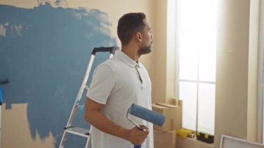 Yeni evin içinde kutular ve merdivenlerle çevrili bir evde resim yapan adam, evin yenilenmesini öneriyor.