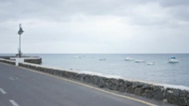 Limanda taştan bir duvar, sokak lambası ve sönmüş tekneleri olan bulanık bir kıyı yolu manzarası lanzarotun bulutlu gökyüzüne, kanarya adalarına, İspanya 'ya karşı.