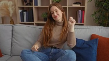 Rahat bir oturma odasında, gri bir kanepede neşeyle dans eden kadın renkli yastıklarla ve arka planda bir kitaplıkla çevrili neşeli bir anı kucaklıyor..