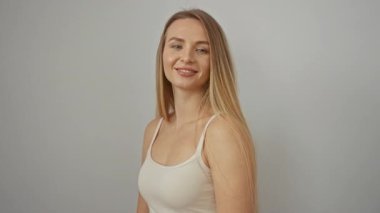Genç bir kadın, özgüvenle gülümsüyor yumuşak beyaz bir arka plana karşı, sarışın ve sakin bir yüz ifadesi sergiliyor, zorlayıcı bir portre için minimalist bir ortamda izole edilmiş..