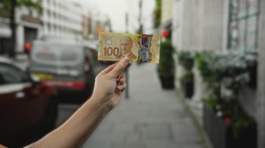 Meşgul bir şehir caddesinde yüz dolarlık Kanada banknotuyla el ele tutuşmak, canlı bir şehir hayatı ve açık hava finans kavramı sergiliyor..