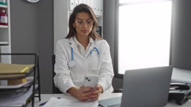 Doktor kadın hastane ofisinde steteskop ve laptopla iletişim ve profesyonel çevreyi gösteren akıllı telefon kullanıyor..