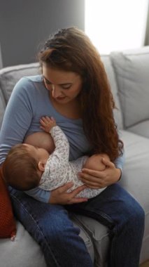 Anne bebeğini rahat bir oturma odasında emziriyor, aile sevgisini somutlaştırıyor ve ev ortamında besleniyor..