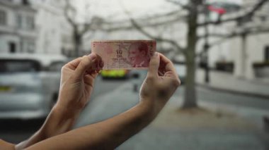 Arka planda bulanık bir şehir caddesi olan 10 lira banknot tutan eller, şehir ortamında para birimini açık havada gösteriyor..