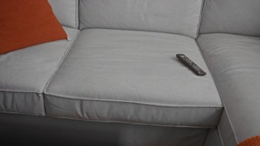 Kot pantolonlu genç adam modern bir kanepede uzaktan kumanda kullanıyor samimi bir oturma odasında rahat bir dekor ve davetkar bir ortam hazırlıyor..