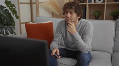 Uzaktan kumandalı genç adam, rahat bir evin iç tarafında, rahat bir atmosferi vurgulayarak, şık dekorlar ve bitkilerle çevrili, düşünceli bir şekilde televizyon seyrediyor..