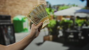 Bir şehir caddesindeki açık hava restoranının terasında Norveçli kron banknotları tutan bir erkek..