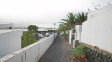 Lanzarote 'daki bulanık yürüyüş yolu, odağını kaybetmiş beyaz duvarlar, palmiye ağaçları ve kanarya adalarının uzak manzarası..