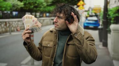 Bir şehir caddesinde elinde Türk lirası tutan İspanyol bir adam el pençe divan dinliyor, merak ve entrika saçıyor..