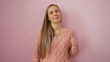 Pembe kazakla gülümseyen bir kadın pembe arka planda olumlu duygu ve mutluluğu temsil eden başparmaklarını kaldırıyor.