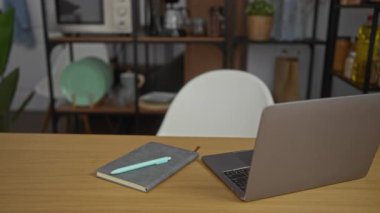 Ofiste çalışan genç bir adam, dizüstü bilgisayarı ve gazeteleri olan iyi düzenlenmiş bir odada, bir masada bardak tutarken süveter giyen.