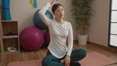 Yoga yapan bir kadın spor salonundaki minderde egzersiz topları ve bitkilerle rahat bir iç mekan fitness ortamı yaratıyor..