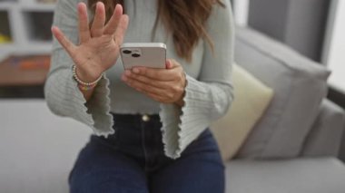 Rahat oturma odasında akıllı telefon kullanan bir kadın modern dekor ve günlük kıyafet giydirme teknolojisi ve boş zamanlarında.