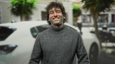 Şehir manzarası ve arabalarla çevrili bir caddede kendini neşeli bir ifadeyle kucaklayan genç adam, dışarıda mutluluk ve pozitifliği resmediyor..