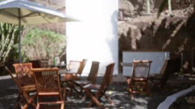 Güneşli bir lanzarot arka planında şemsiyelerin altına kurulmuş ahşap sandalyeler ve masalarla bulanık hava sahnesi, bokeh etkisi ve odaklanmış arka planı gösteriyor..