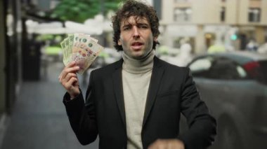 Arjantin pesoları tutan İspanyol adam işlek şehir caddesinde duruyor, sinsice başını sallıyor ve modern şehir zemininde anlaşmazlık içinde parmağını kaldırıyor..