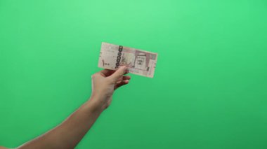 Suudi Arabistan riyal banknotunu izole edilmiş yeşil arka plan duvarına karşı tutan adam, para ve maliyeyi vurguluyor.