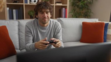 Evdeki rahat yaşam tarzını gösteren, şık dekorlar ve yastıklarla çevrili, keyifli bir ifadeyle, rahat oturma odasında video oyunları oynayan bir adam..