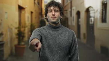Gri kazaklı genç adam gündüz vakti dar şehir sokaklarında geleneksel mimari ve sonbahar atmosferiyle şehir ortamında jest iletişimini temsil ediyor.