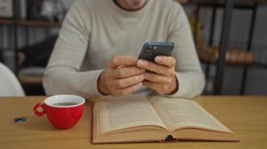 Ofiste kahve içen ve kitabı açık akıllı telefon kullanan olgun bir adam.
