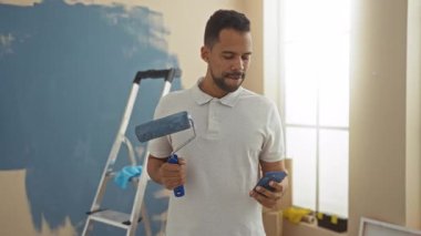 Kapalı alanda resim yapan genç bir adam yeni evde merdiven başında telefonları kontrol ediyor..