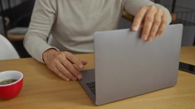 Normal atmosfer teknolojisi olan bir ofiste dizüstü bilgisayar kullanan ve modern mutfak aletleri ve düzenli çalışma alanı etrafında çalışmaya odaklanan olgun bir adam..