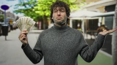 Bir elinde Rus rublesi olan İspanyol bir adam, diğer elinde de düşünceli bir ifadeyle gri bir kazak giymiş, kentsel bir mali bağlam yakalıyor..