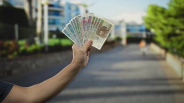 Elinde Polonya parası olan bir adam şehir sokaklarının arka planında gün ışığında bulanık binalar ve ağaçlar tutuyor..