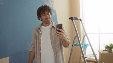 Oturma odasındaki duvarları boyarken gülümseyen bir adam yeni apartman dekorunu göstererek neşeli ve modern bir ortam yaratıyor..