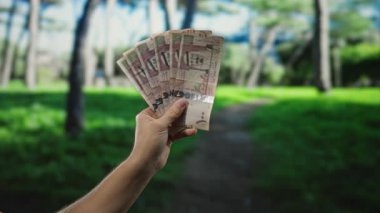 Açık hava parkı ortamında Suudi riyal banknotları tutan adam doğal yeşil bir geçmişi olan döviz kurunu vurguluyor. Ekonomik büyümeyi işaret ediyor..