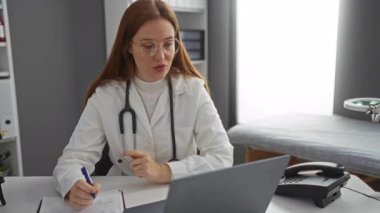 Klinikte steteskop takan bir kadın, bilgisayarlı bir masaya notlar yazıyor ve modern bir muayenehanede telefonla konuşuyor..
