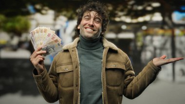 Bir elinde Türk lirası banknotları tutarken, şehrin sokaklarında gülümseyen İspanyol bir adam, şehir ortamında kendine güvenen bir jest yapıyor..