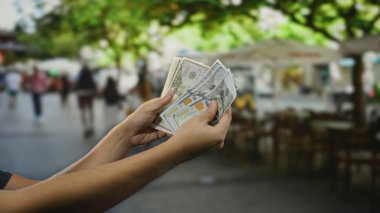 Bir restoranın terasında arka planında hareketli bir kahve seti olan hareketli bir şehir sokağında dikilmiş Amerikan dolarlarını elinde tutan bir adam..