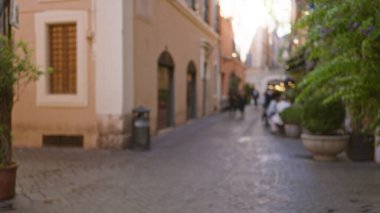 Roma 'da, tarihi binaların ve yemyeşil alanların arasında yürüyen ve İtalyan kentsel hayatının özünü yakalayan odaksız insanların olduğu bir caddenin bulanık görüntüsü..