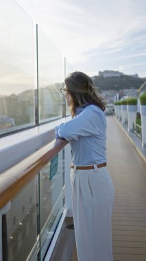 Uzaktaki şehir manzaralı rıhtıma bakan kadın huzurlu yolculuk anını yansıtıyor..