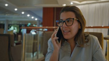 Lüks bar salonunda konuşan bir kadın zarif iç dekorasyon ve sıcak ışıklandırma ayarlarıyla modern sofistike ve enerjik gençliği sergiliyor..